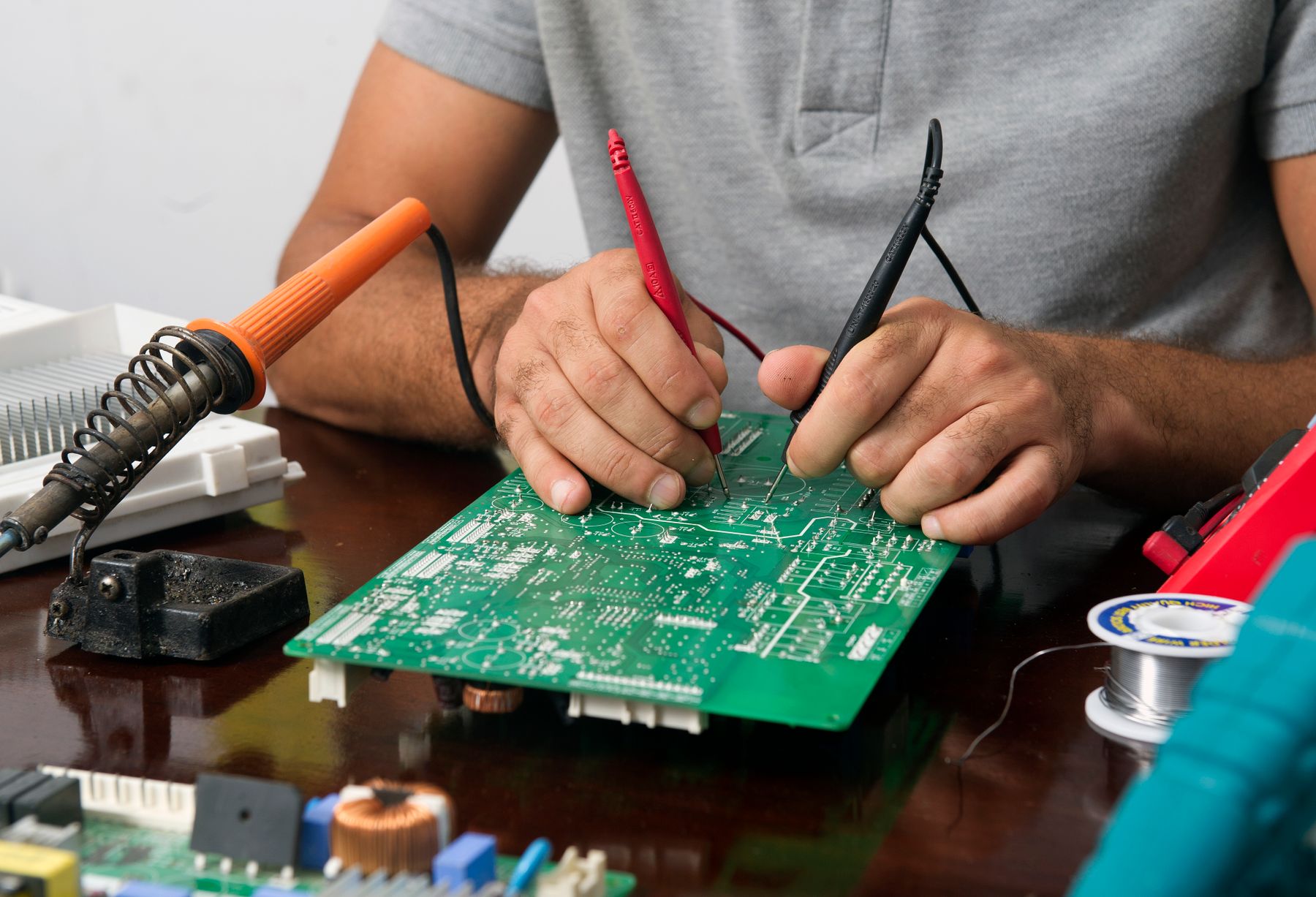 Technician testing a printed circuit board with multimeter probes on a workbench